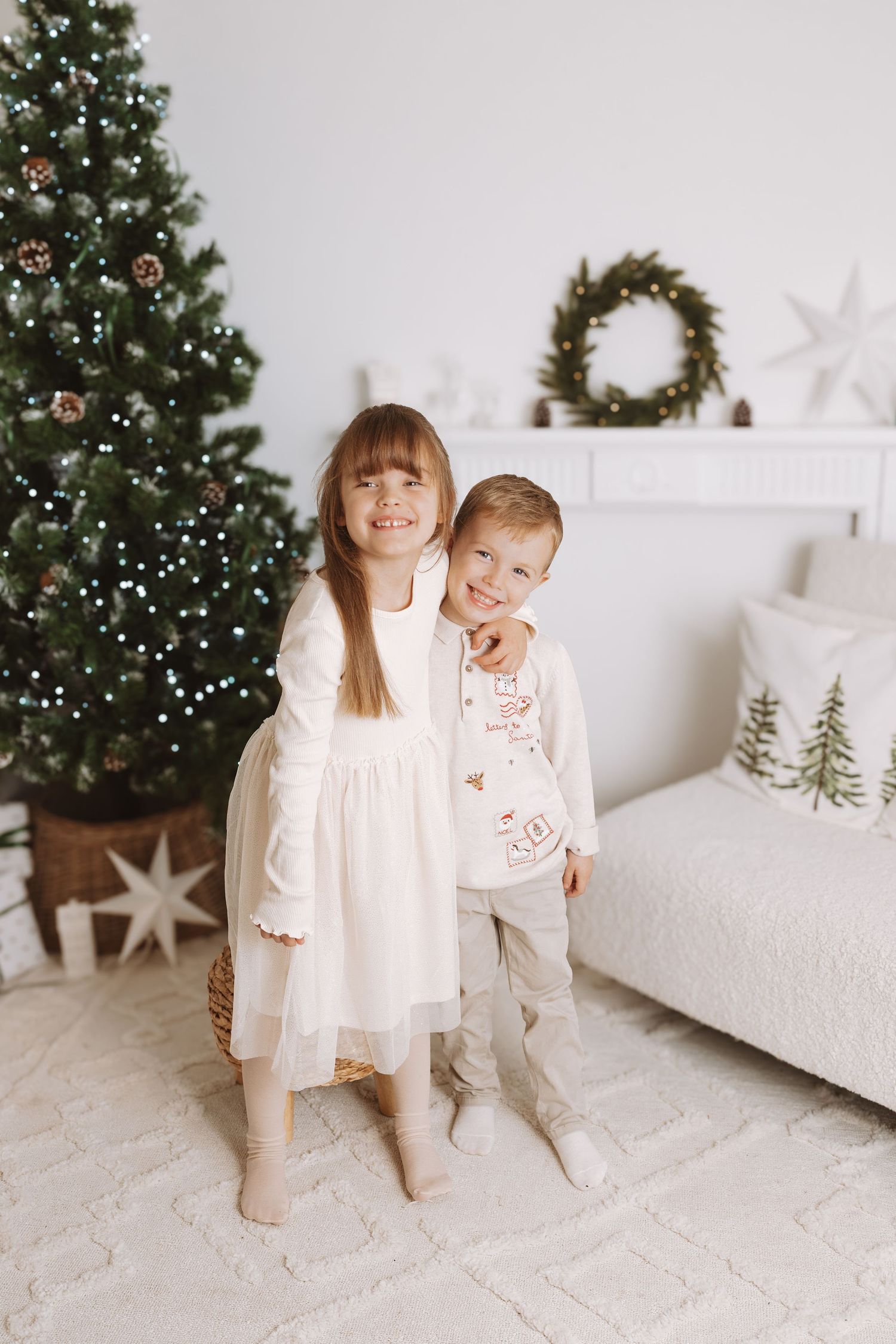 A white decorated studio setting with floral arrangements and a small white stepstool against a light backdrop.