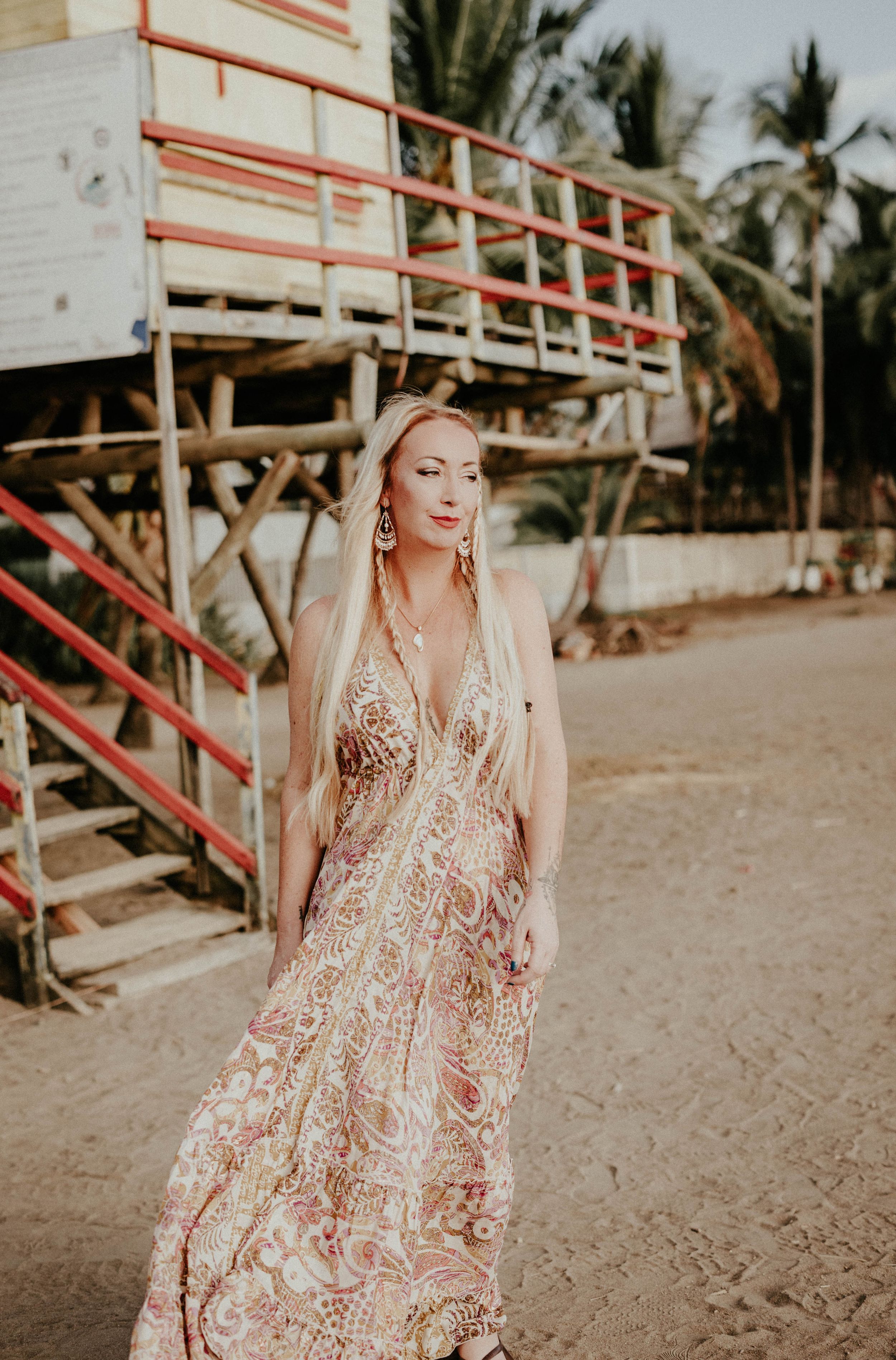 A person in a floral pink dress poses near a wooden beach boardwalk during sunset.