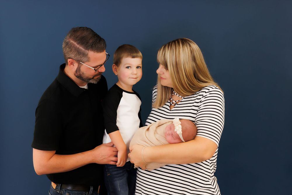 Family portrait with young child and newborn against blue studio background.