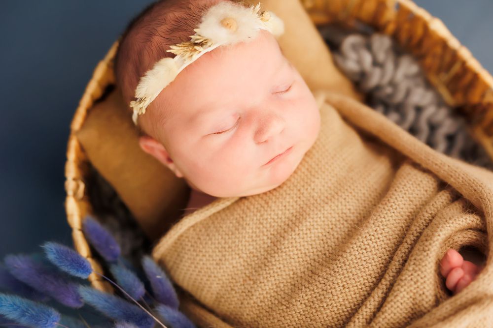 Sleeping newborn wrapped in burlap blanket resting in cozy basket with delicate headband.
