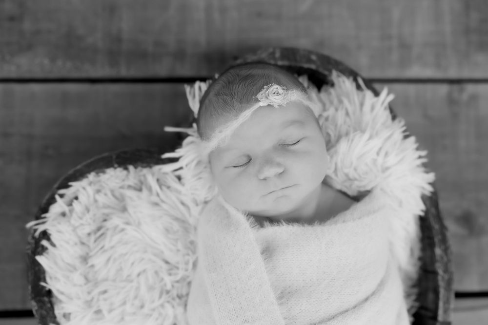 A peaceful baby rests on soft white feathers in a vintage black and white photo.