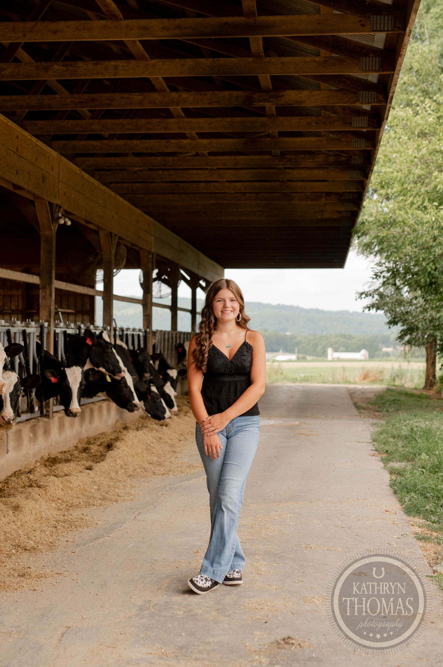 A casual portrait in front of a dairy barn with cows visible in the background.