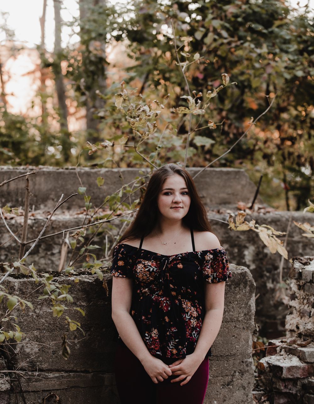Artistic portrait series against rustic stone wall with floral dress in warm autumn lighting.