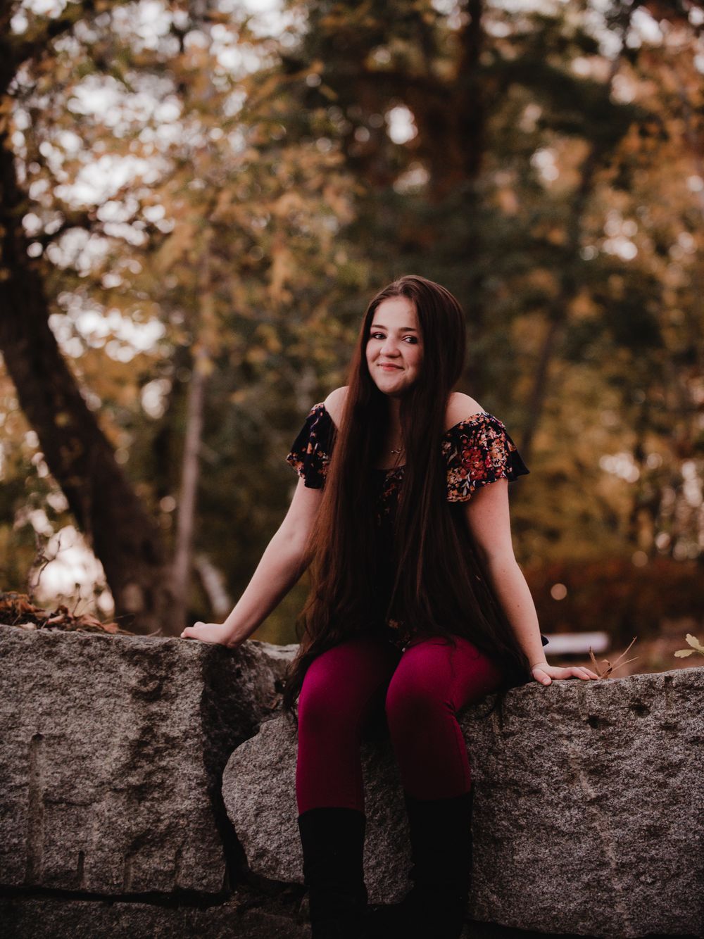 Autumn outdoor portrait session with floral off-shoulder dress against stone wall and golden foliage.