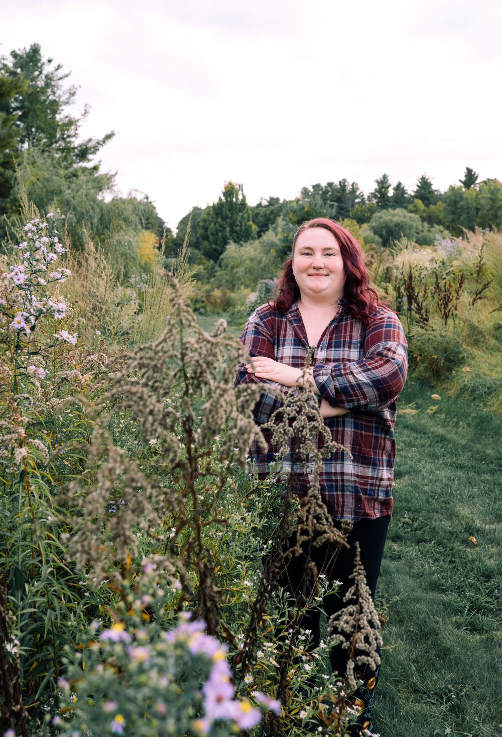 Person standing in a wildflower meadow wearing a plaid flannel shirt on an autumn day.