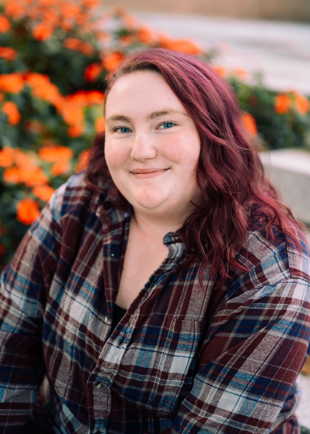 Person in plaid shirt smiling against backdrop of vibrant orange flowers.