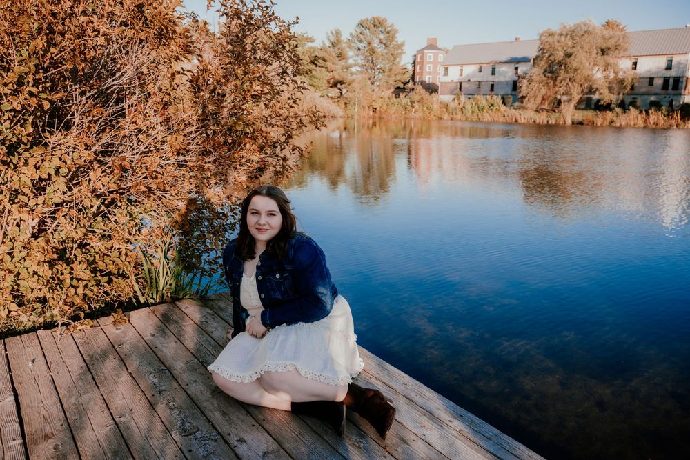 Person sitting on wooden dock overlooking autumn lake during sunset.