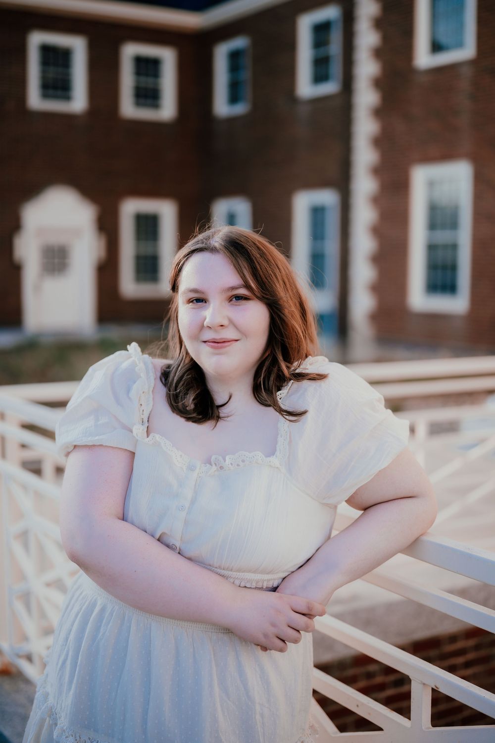 A person in a white dress sits on outdoor white benches near a brick building.