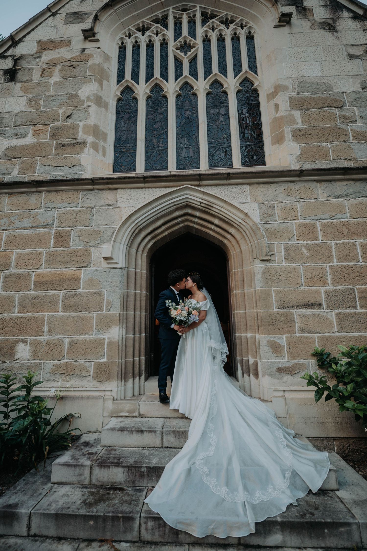 A couple shares an intimate moment under a Gothic church archway with a dramatic flowing wedding dress train.