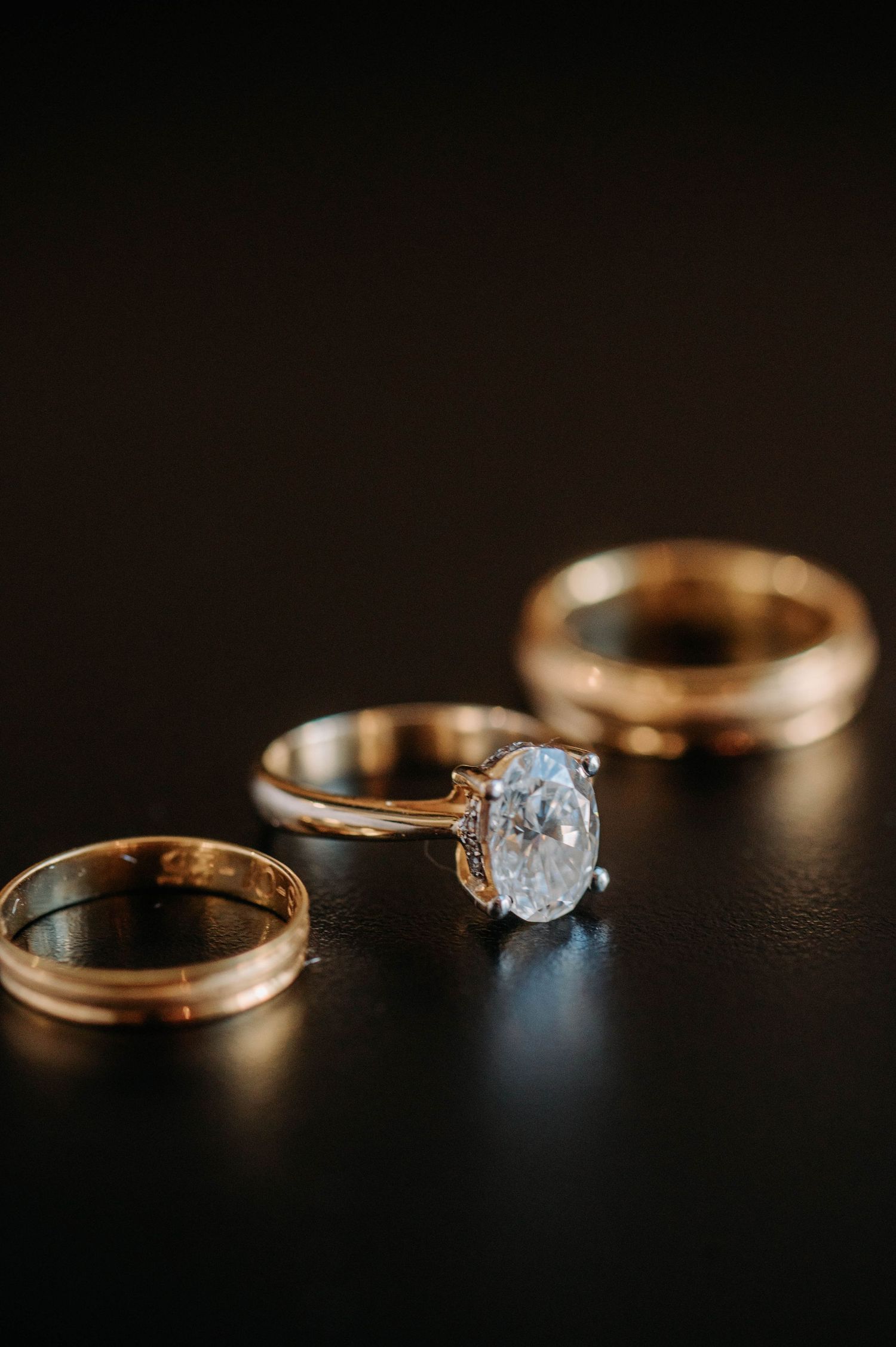 Close-up of three gold wedding rings with diamond engagement ring on dark background.