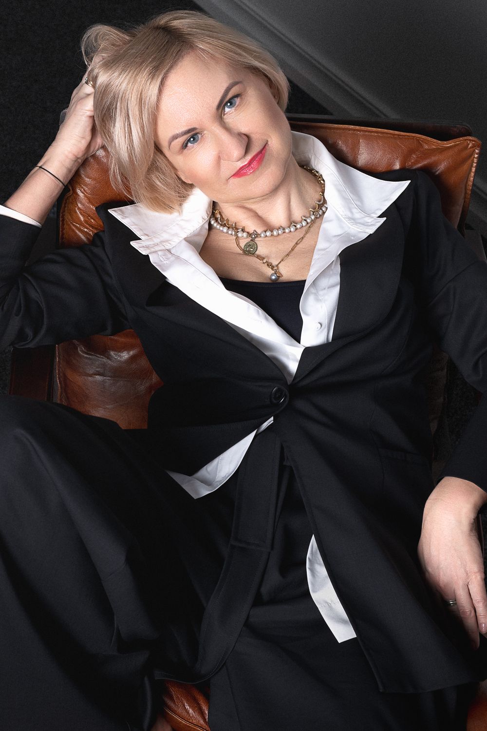 Stylish fashion poses on leather furniture wearing black suit and white collar.
