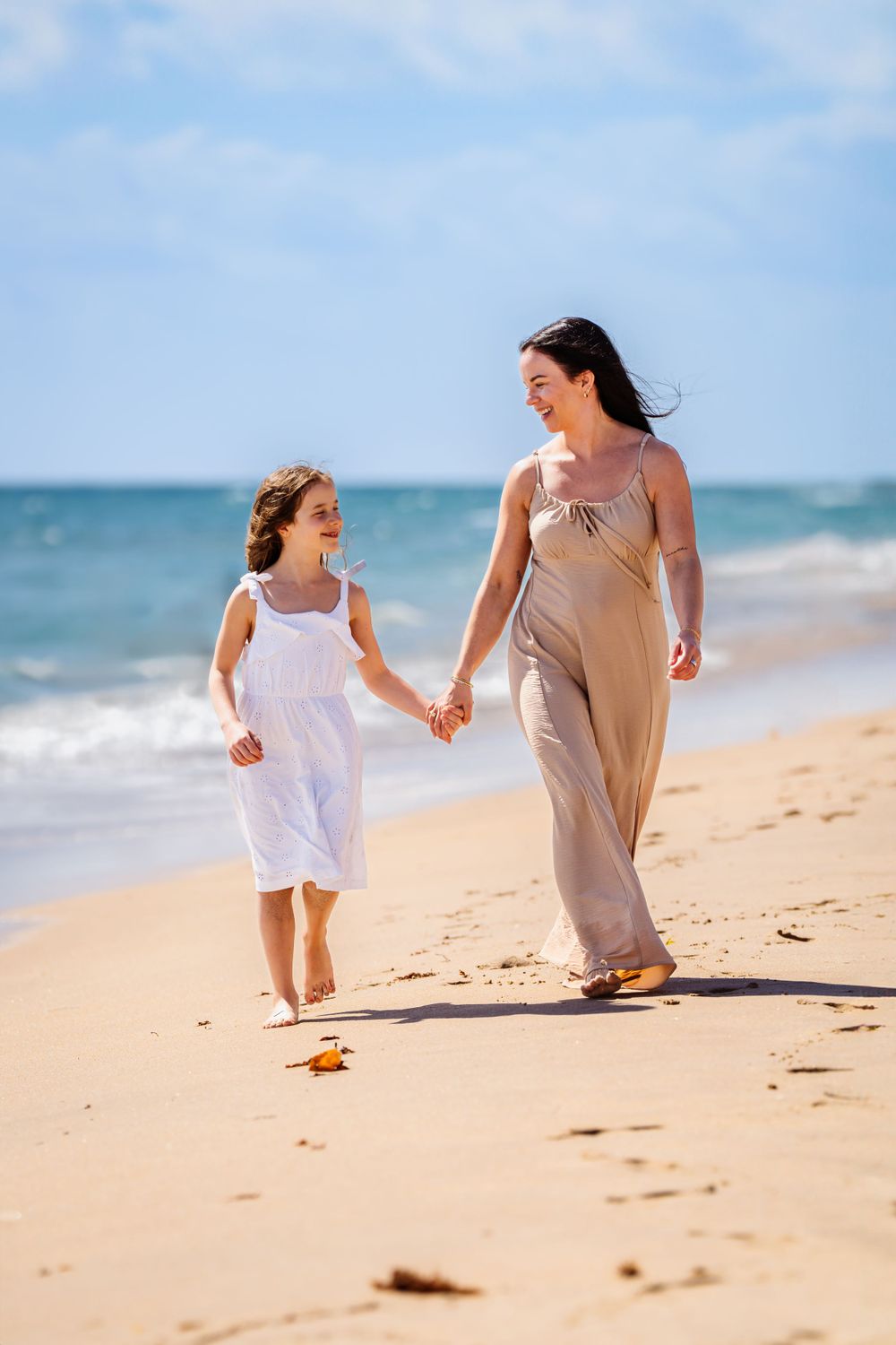 Mother and daughter running playfully together along sandy beach shoreline.
