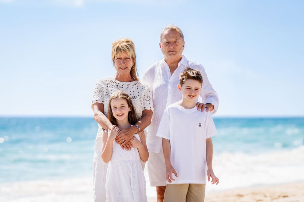 Family group photo on tropical beach with everyone dressed in white casual clothing.