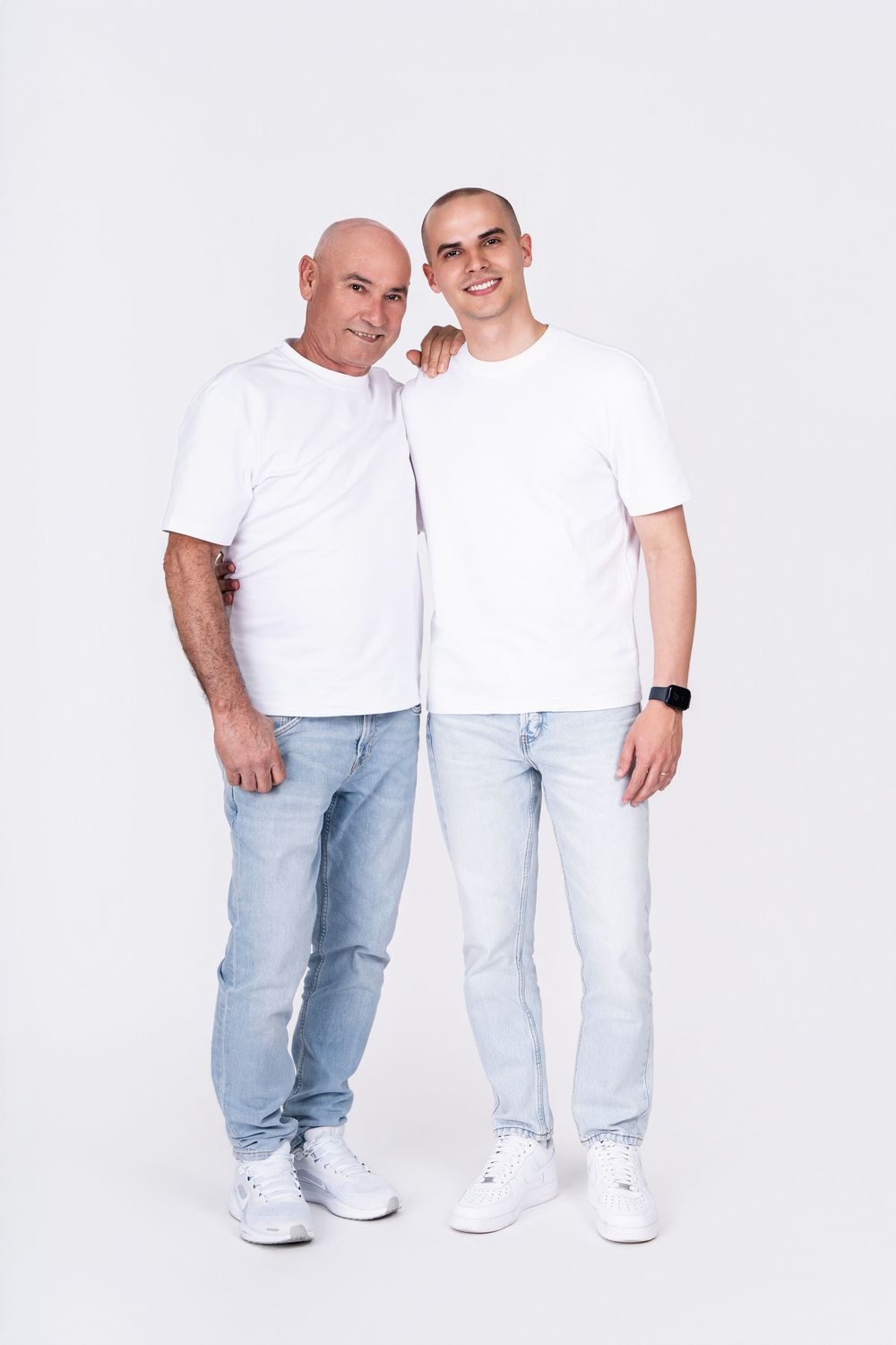 Two people in matching white t-shirts and light jeans pose together against a white backdrop.