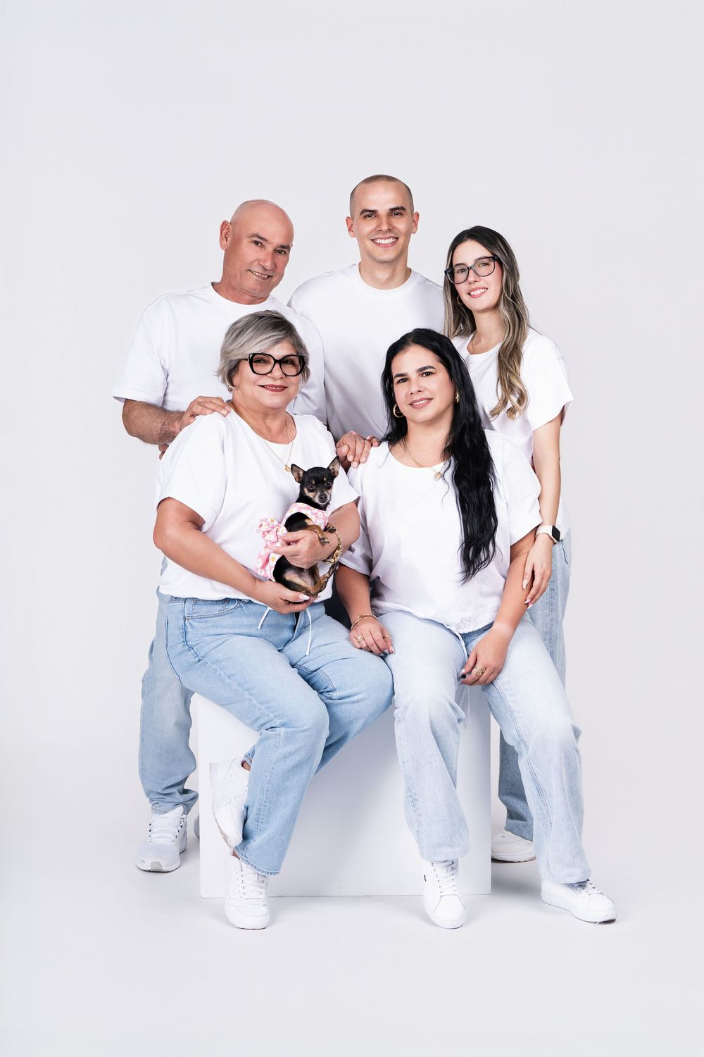 Family portrait with small dog sitting together in matching white and denim outfits.