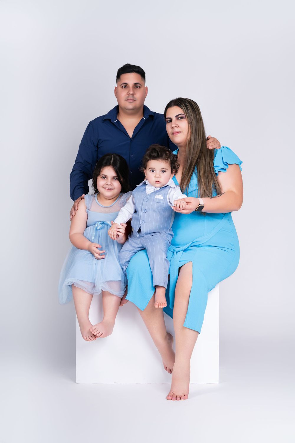 Family portrait with parents and children in blue and white outfits on white backdrop.