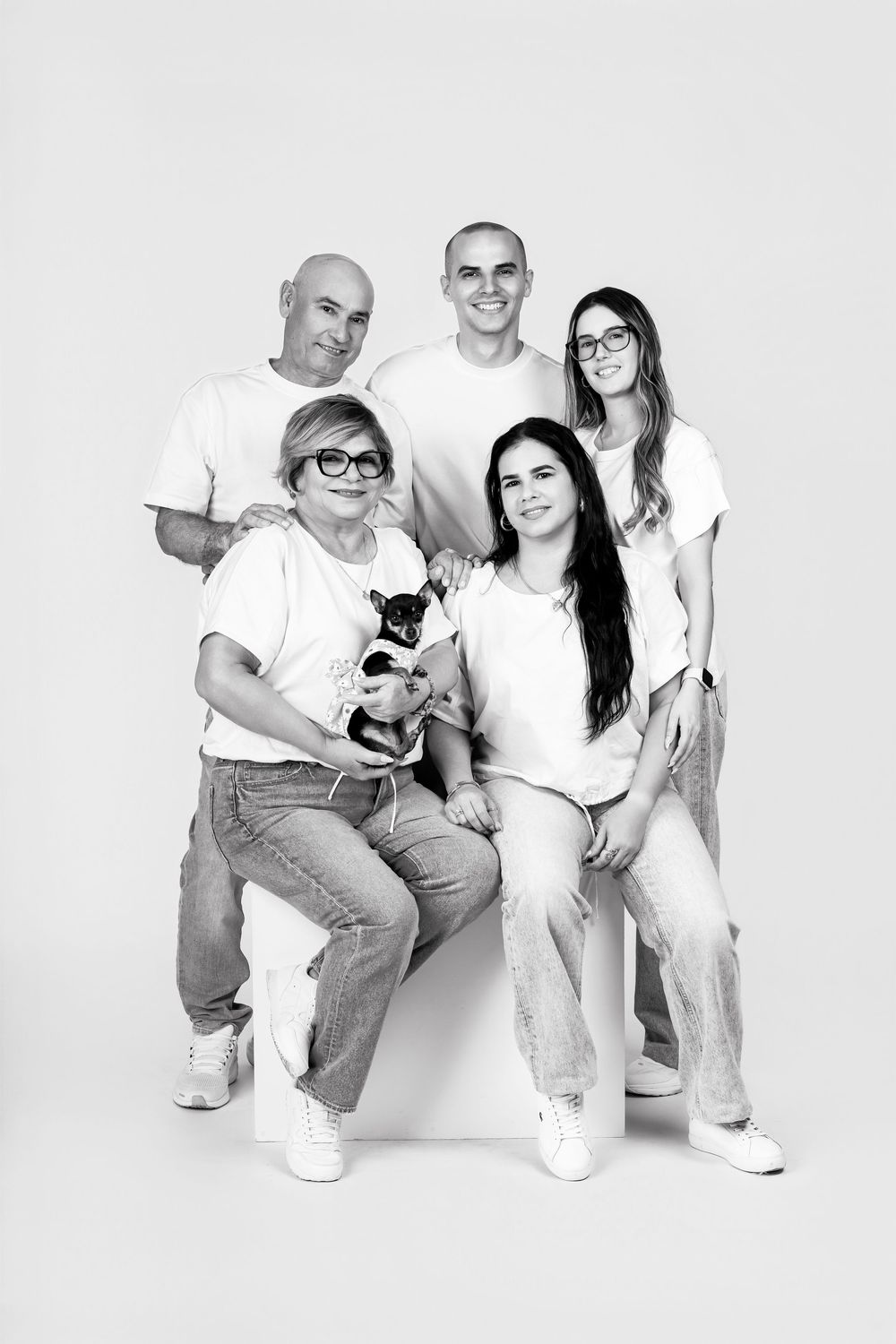Studio portrait of family with small pet dog wearing matching white shirts and jeans.