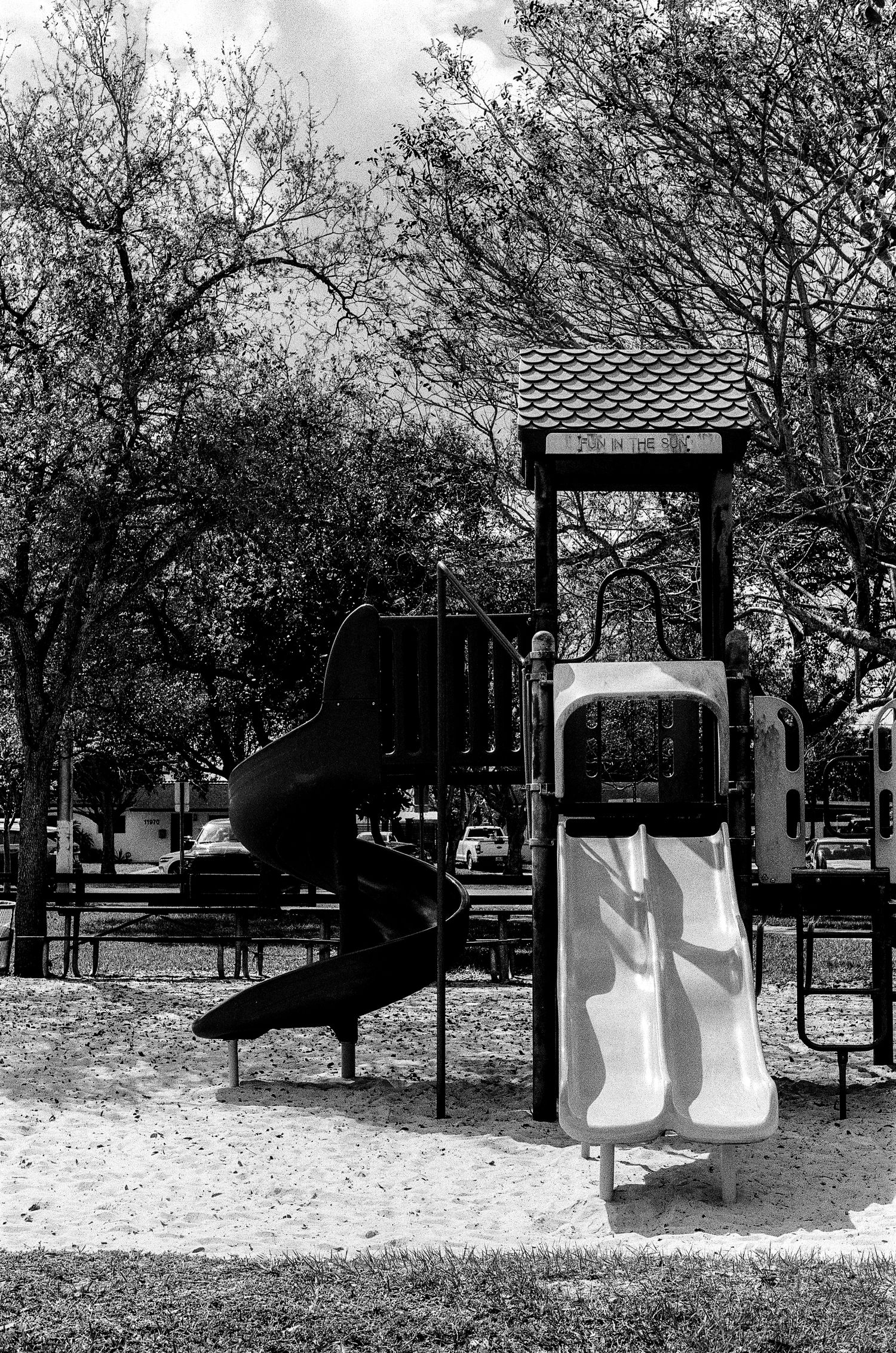 A black and white photograph of an empty playground with a twisting slide and climbing structure casting shadows.