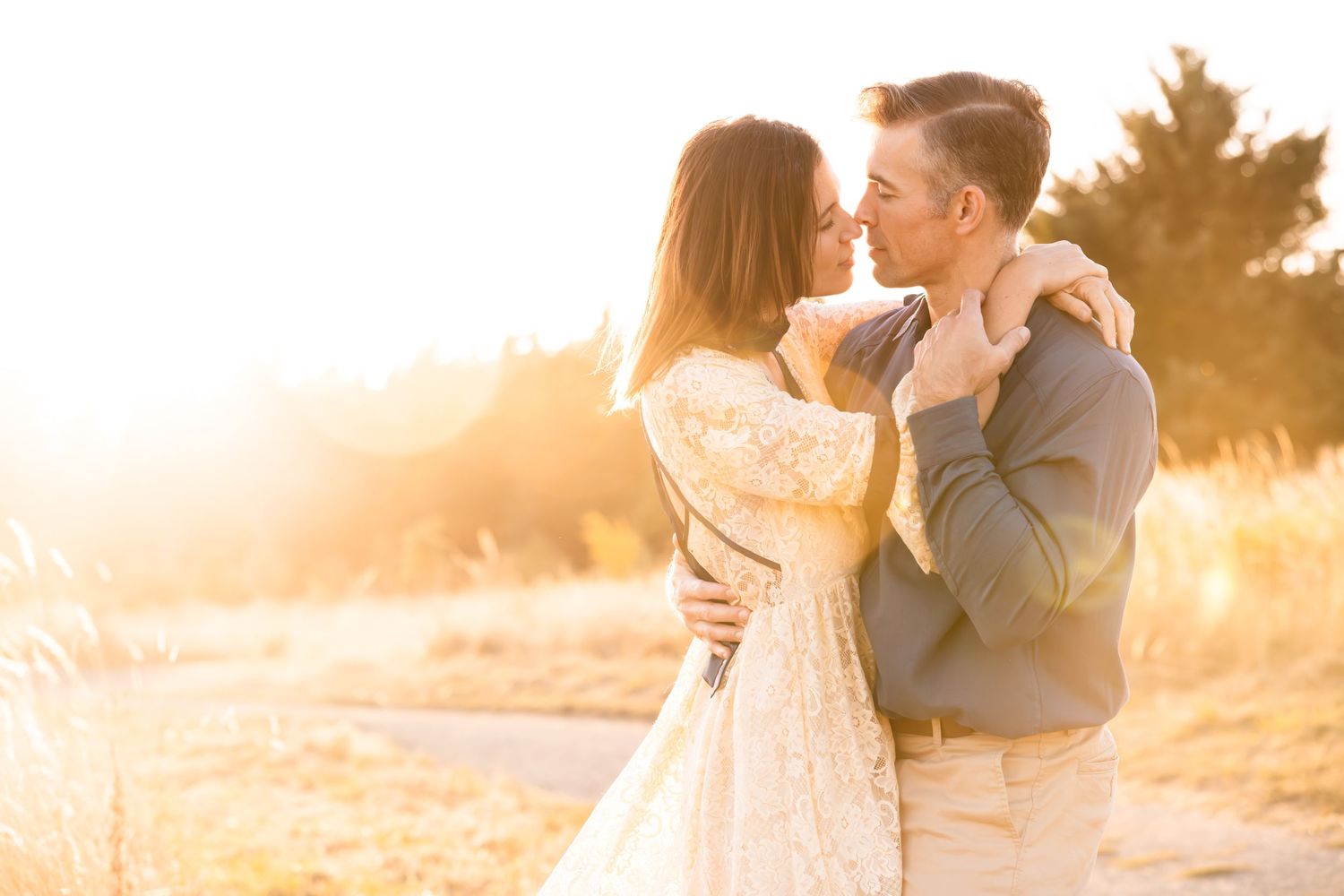 Romantic couple embracing in a golden sunlit field during sunset.