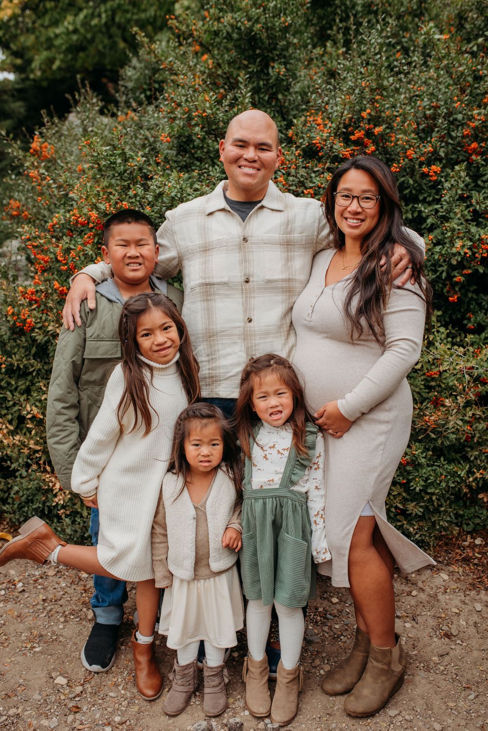 Happy Asian family of six posing outdoors with colorful orange berry bushes in background.