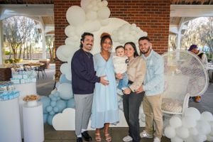 Baby shower celebration with blue and white balloon arch decorations against a brick wall backdrop.
