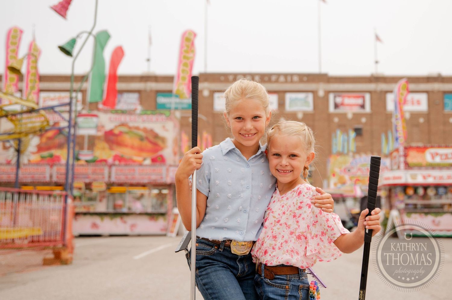 Two exhibitors share a moment at a county fair surrounded by colorful carnival decorations.