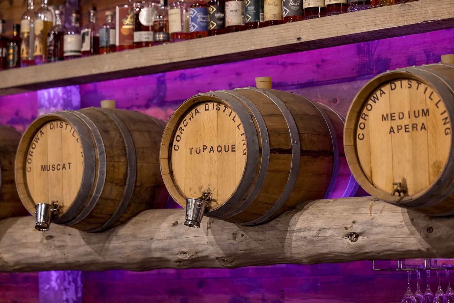 Three wooden aged whiskey barrels on a shelf illuminated by purple ambient lighting in a bar setting at the Corowa Distillery.