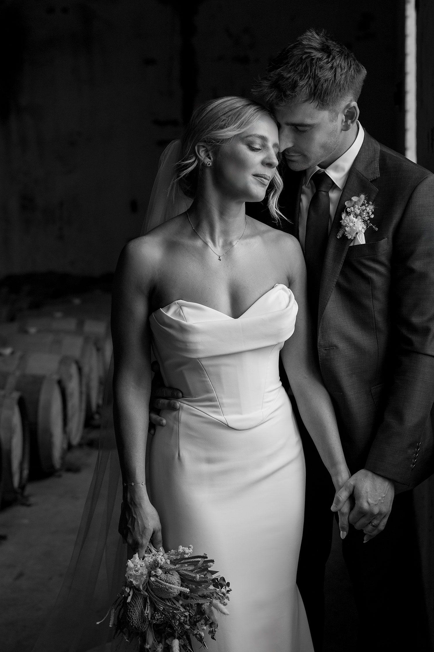 A romantic black and white wedding photo showing a bride in a strapless gown holding a bouquet beside her groom in a dark suit.