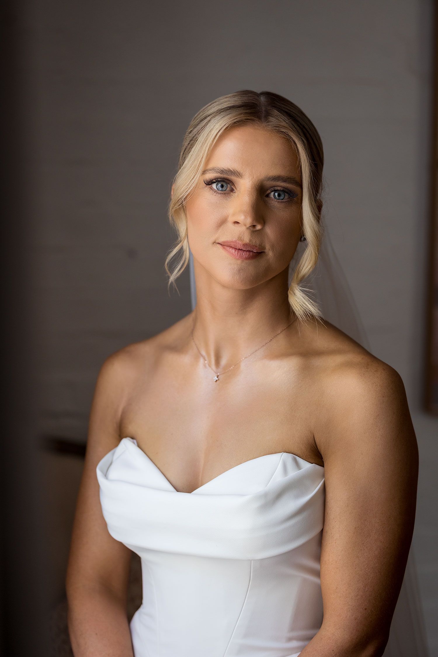 A bride in an elegant strapless white wedding gown holds a dried flower bouquet while standing in a dimly lit room at Quandong Wahgunyah.