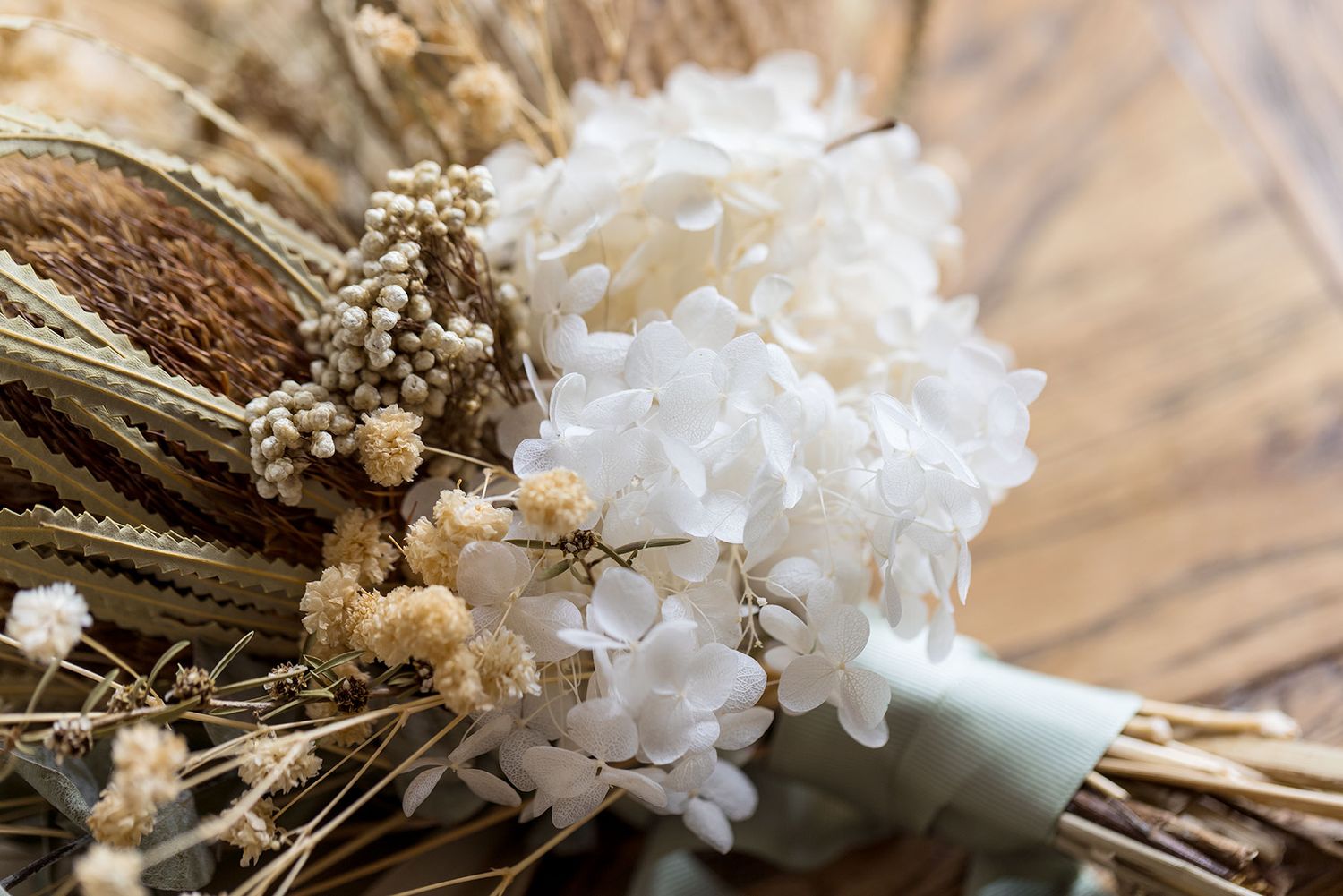 Dried white and beige wedding wildflowers and grasses arranged on rustic wooden surface in soft natural lighting at Quondong Wahgunyah.