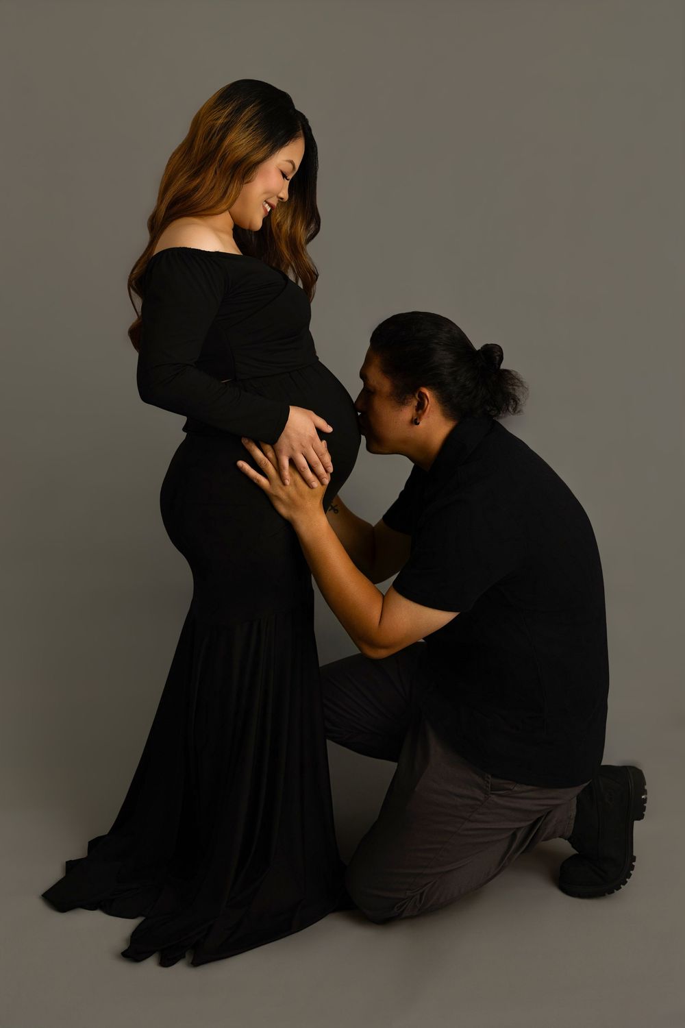 Two people in black and dark clothing pose together against a neutral backdrop in an artistic photo series.
