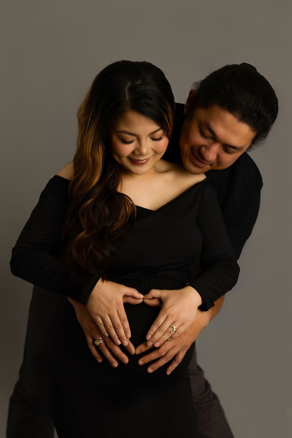 A couple shares a tender embrace against a dark background in a series of romantic maternity photos.