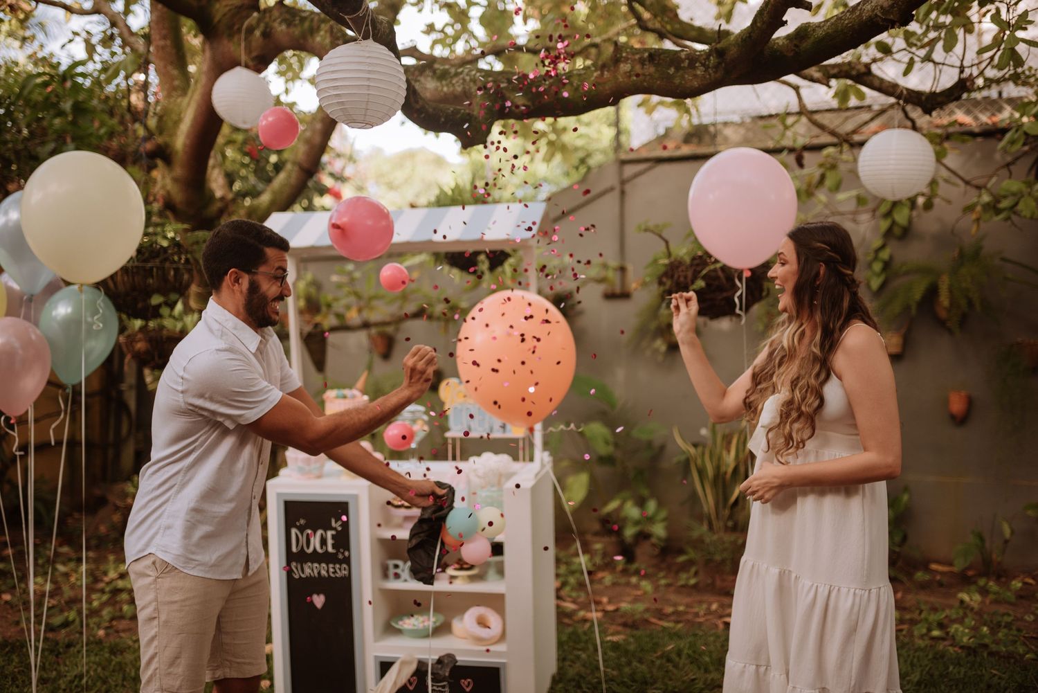Surprise gender reveal moment with couple popping balloon in garden setting.