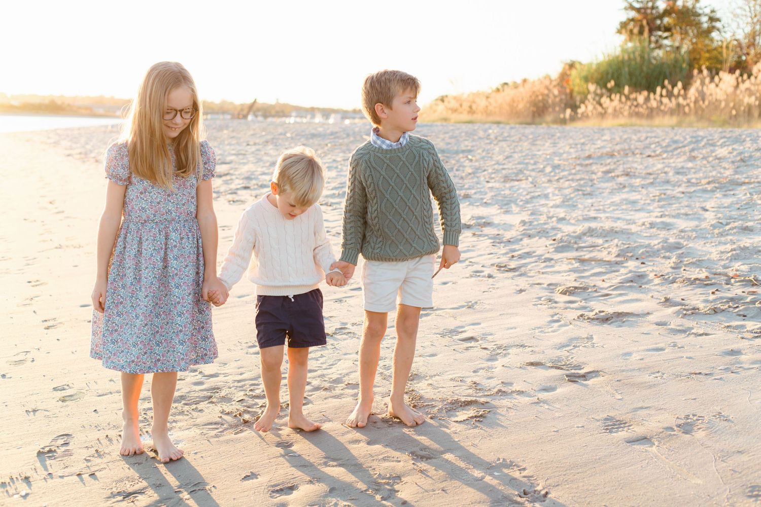 Three siblings walking along Manasquan beach in the fall, dressed in cozy neutral tones with gentle waves in the background.
