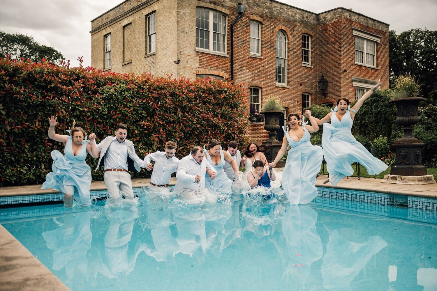 Wedding party makes a splash jumping into pool together with historic mansion in background. Shortmead House