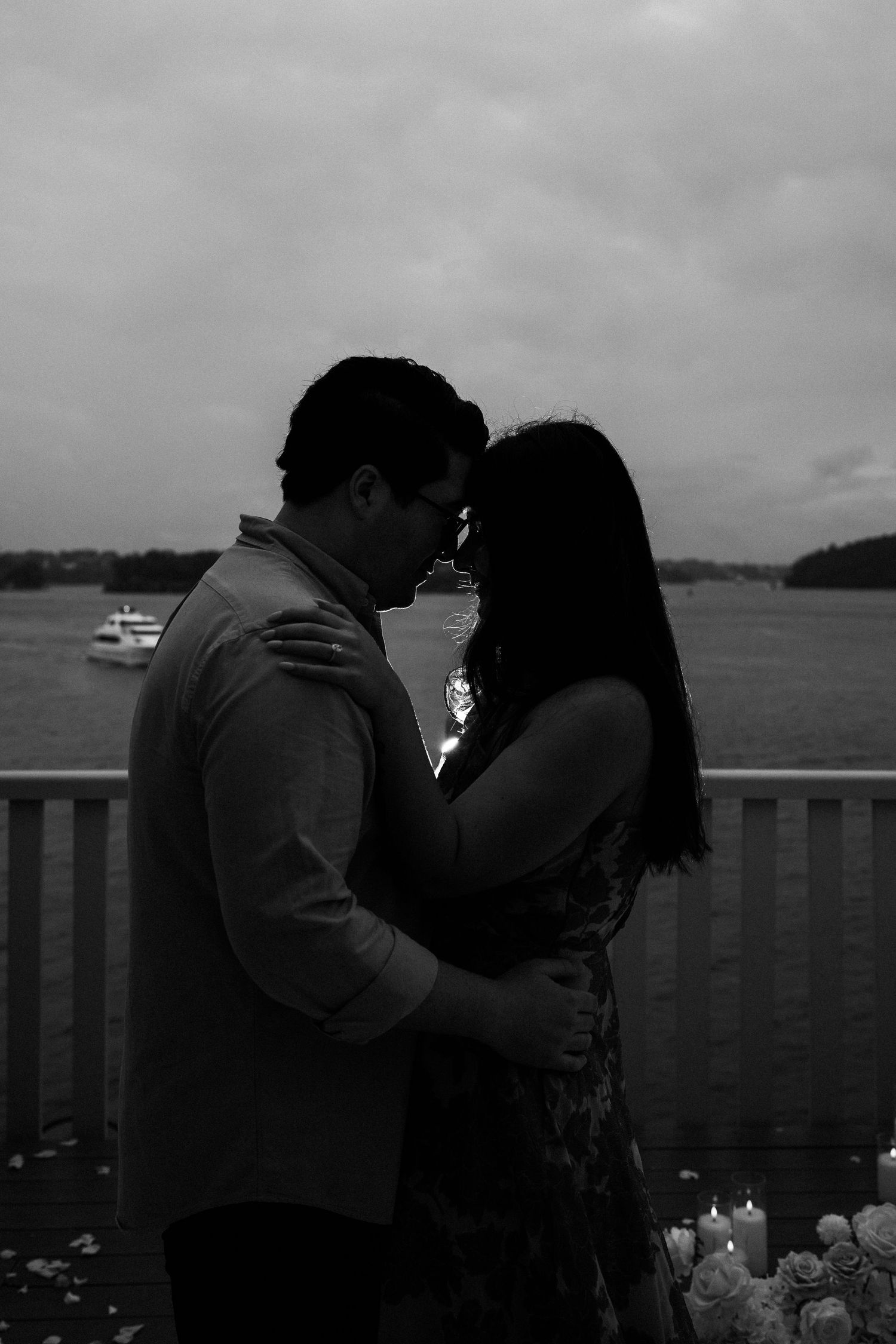 A romantic silhouette of a couple embracing by a waterfront with cloudy skies.