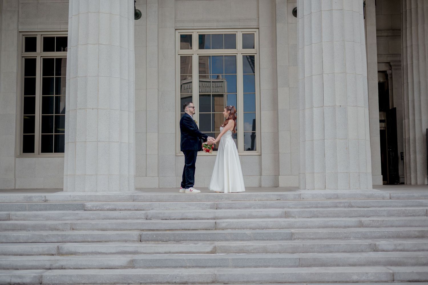 A bride and groom share their first kiss on the grand steps of a white columned courthouse building.