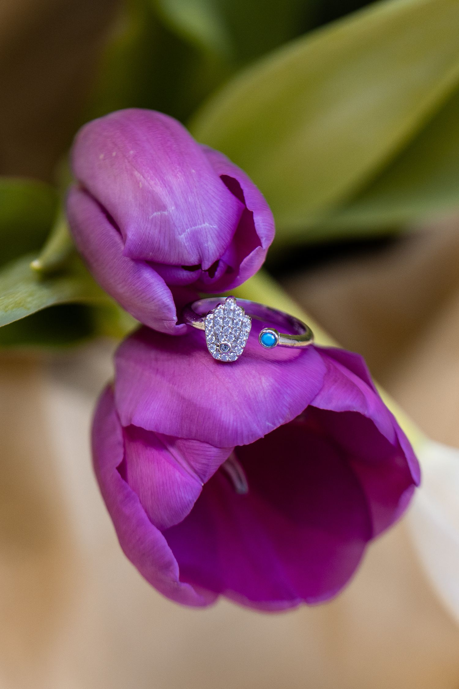 A sparkling diamond engagement ring displayed on a vibrant purple flower petal in a romantic close-up shot.