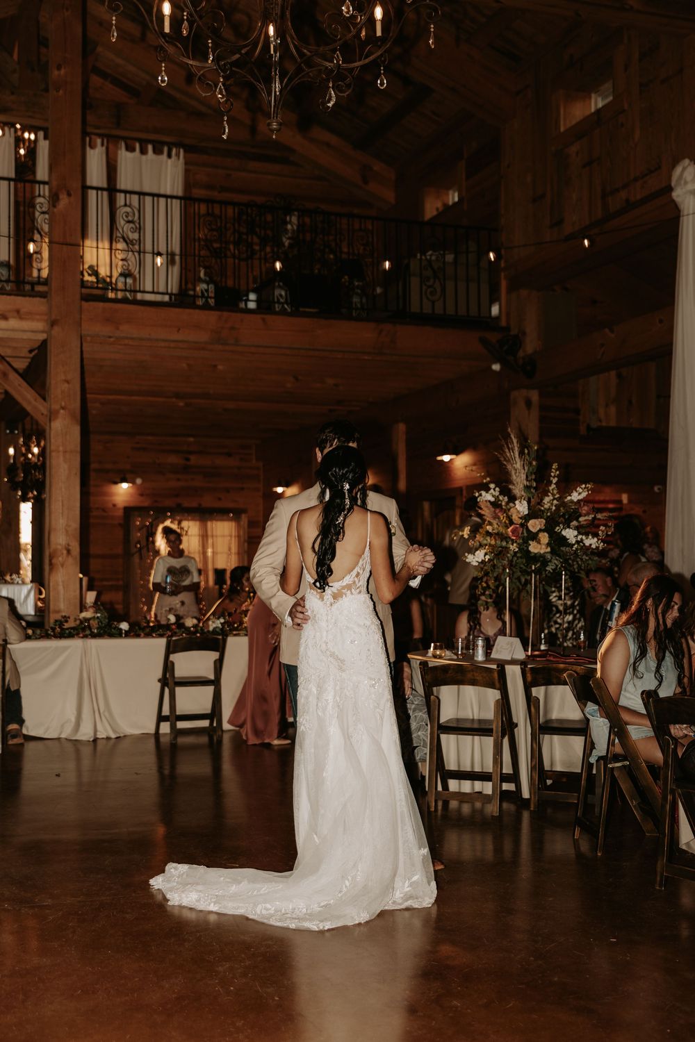 Romantic first dance between newlyweds in a rustic barn venue with string lights overhead.