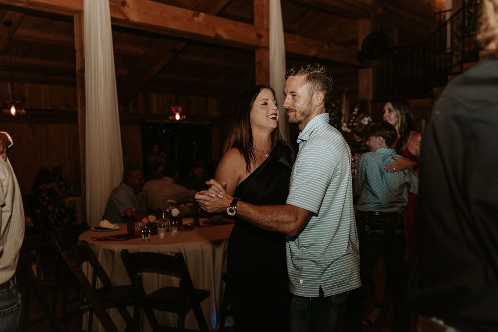 Wedding reception guests dancing and celebrating in a dimly lit rustic venue.