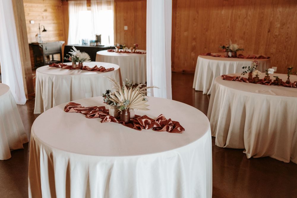 White-clothed round reception tables arranged in a rustic wooden venue with natural lighting.