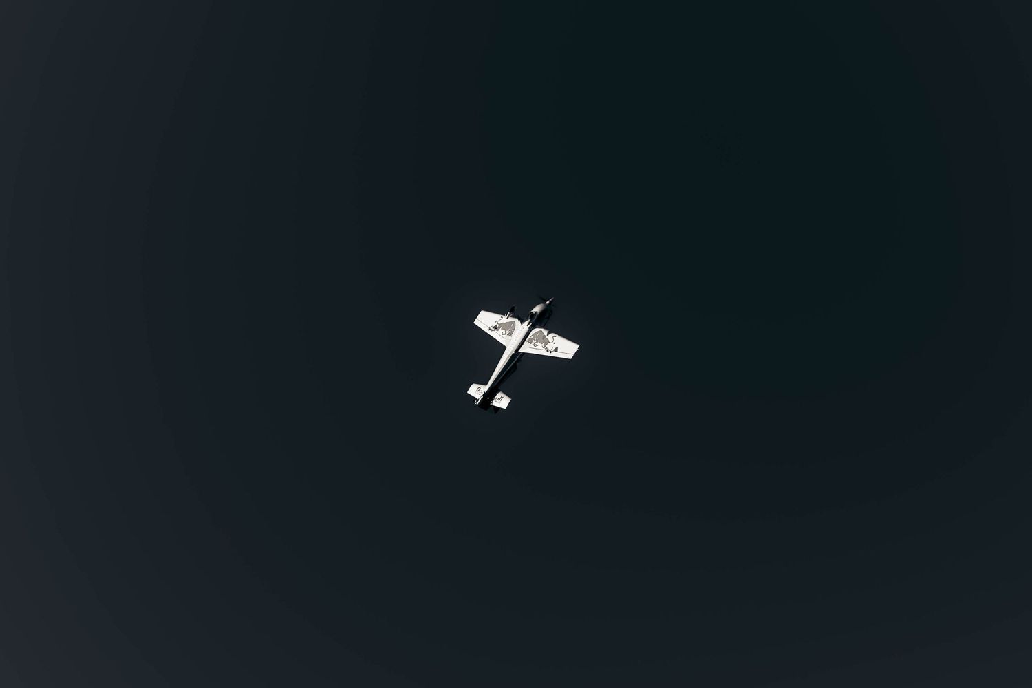 A small white aircraft silhouetted against a dark sky during flight.