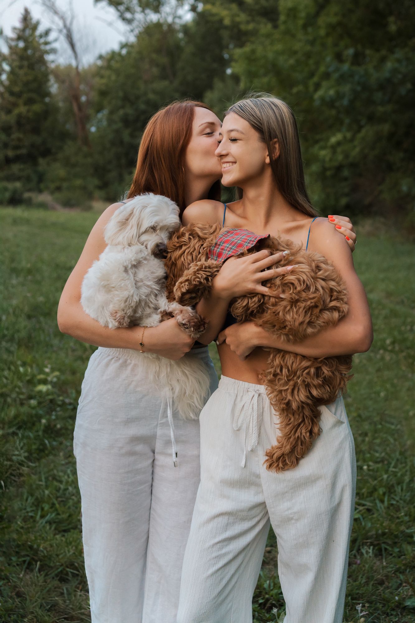 sisters in white outfits share a moments with a fluffy brown goldendoodle dog in rouse hill regional park family photoshoot