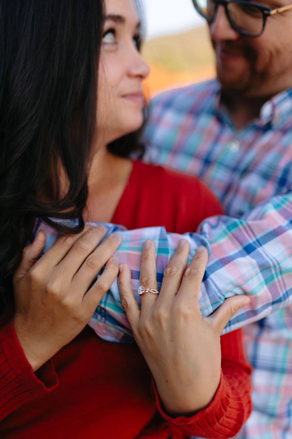 Close-up sequence showing engagement ring on hand against plaid shirt and red sweater in warm sunlight.