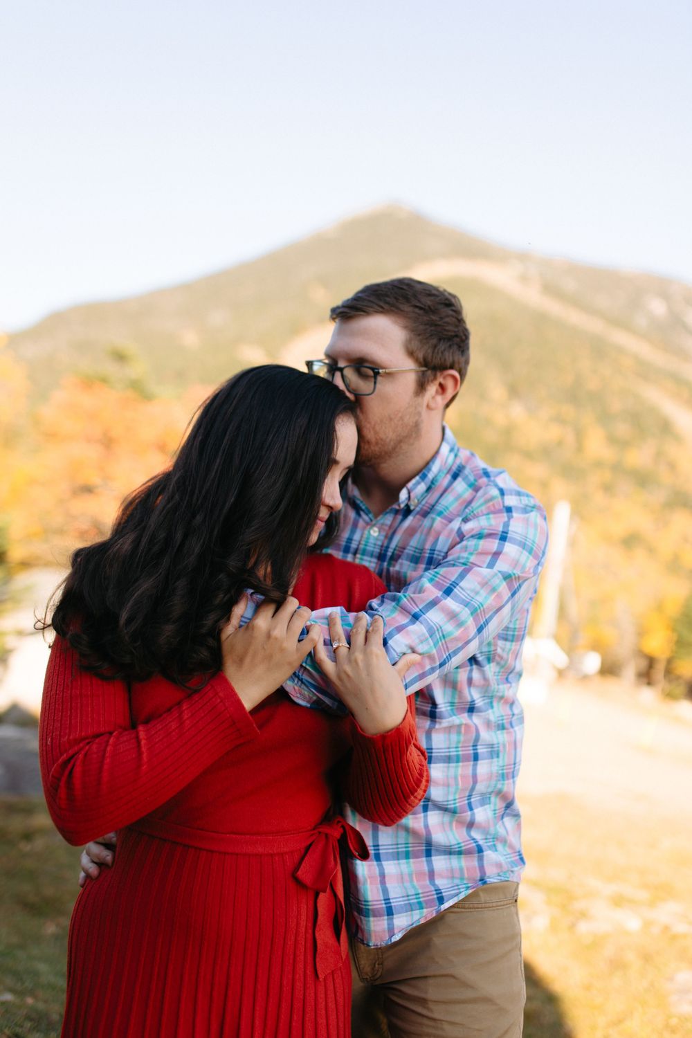 Romantic couple embracing outdoors with mountains in background during golden hour.