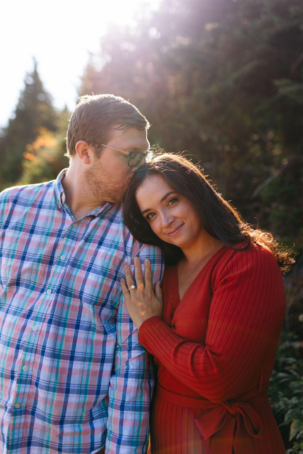 A romantic couple shares tender moments while backlit by golden sunlight in an outdoor setting.