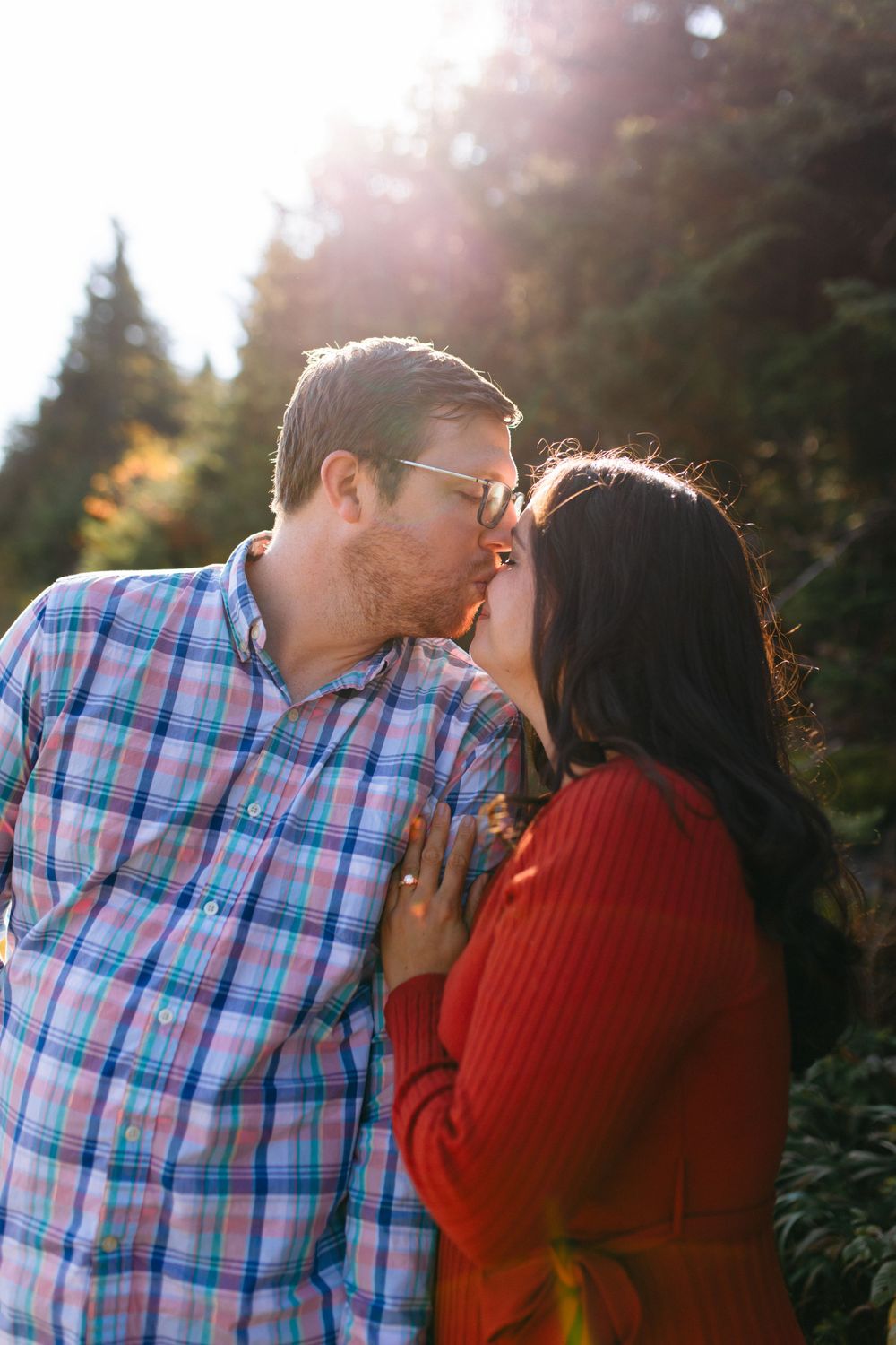 A couple shares tender moments in a sunlit outdoor setting with trees in the background.