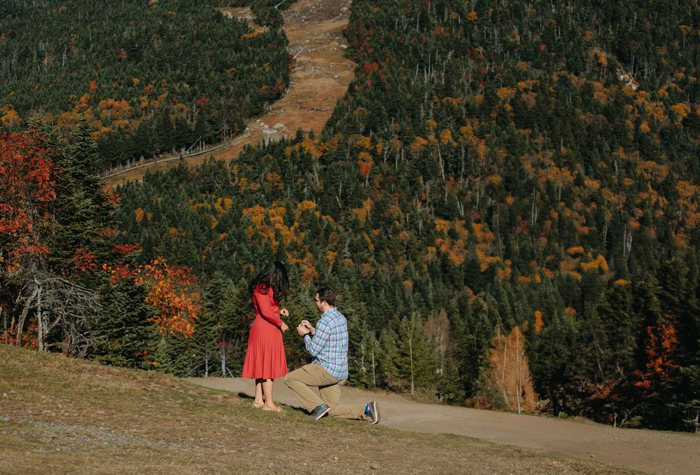 People relax on a mountainside overlooking colorful autumn foliage and rolling hills in the distance.