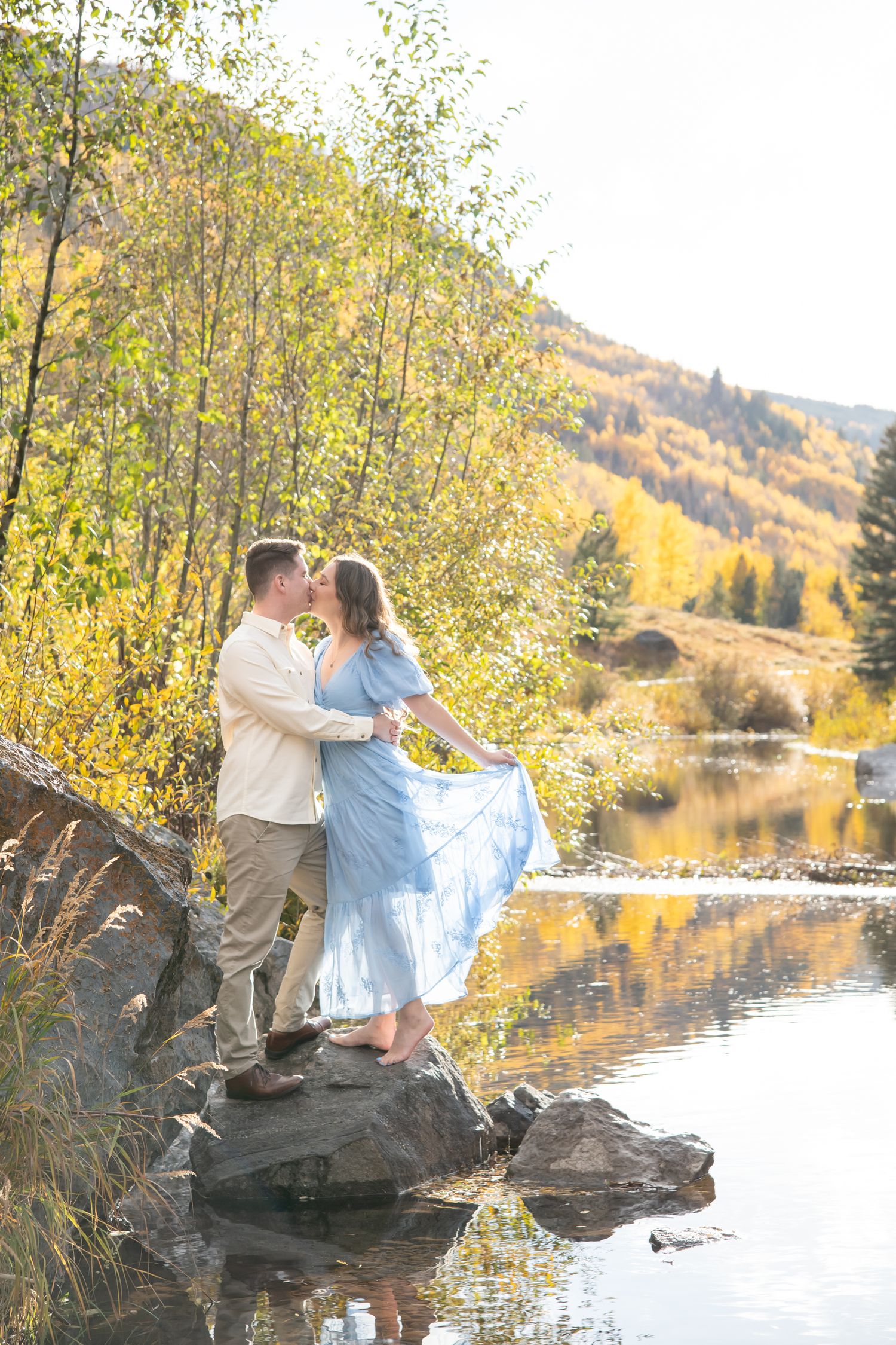 Vail Engagement session on the creek with mountains and golden leaves on the mountains behind them