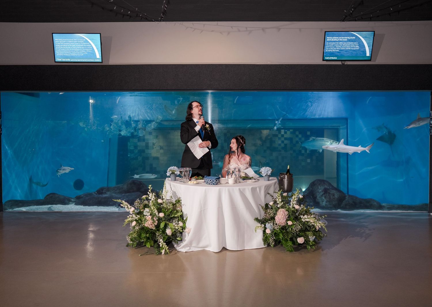 Toledo Zoo & Aquarium Wedding reception setup in front of a large aquarium tank with blue lighting and white decor.